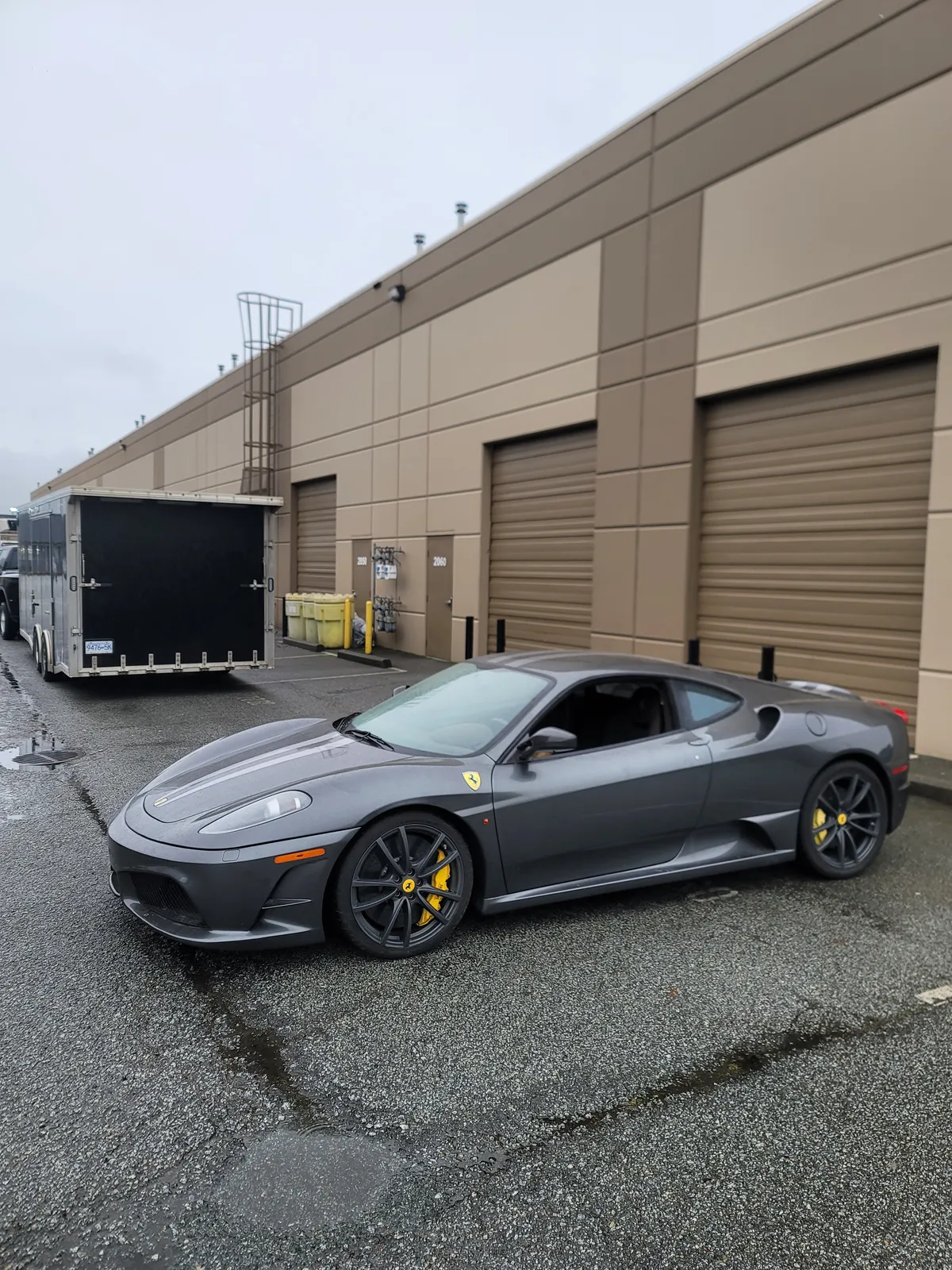 Grey Ferrari F430 staged beside an enclosed trailer before loading.