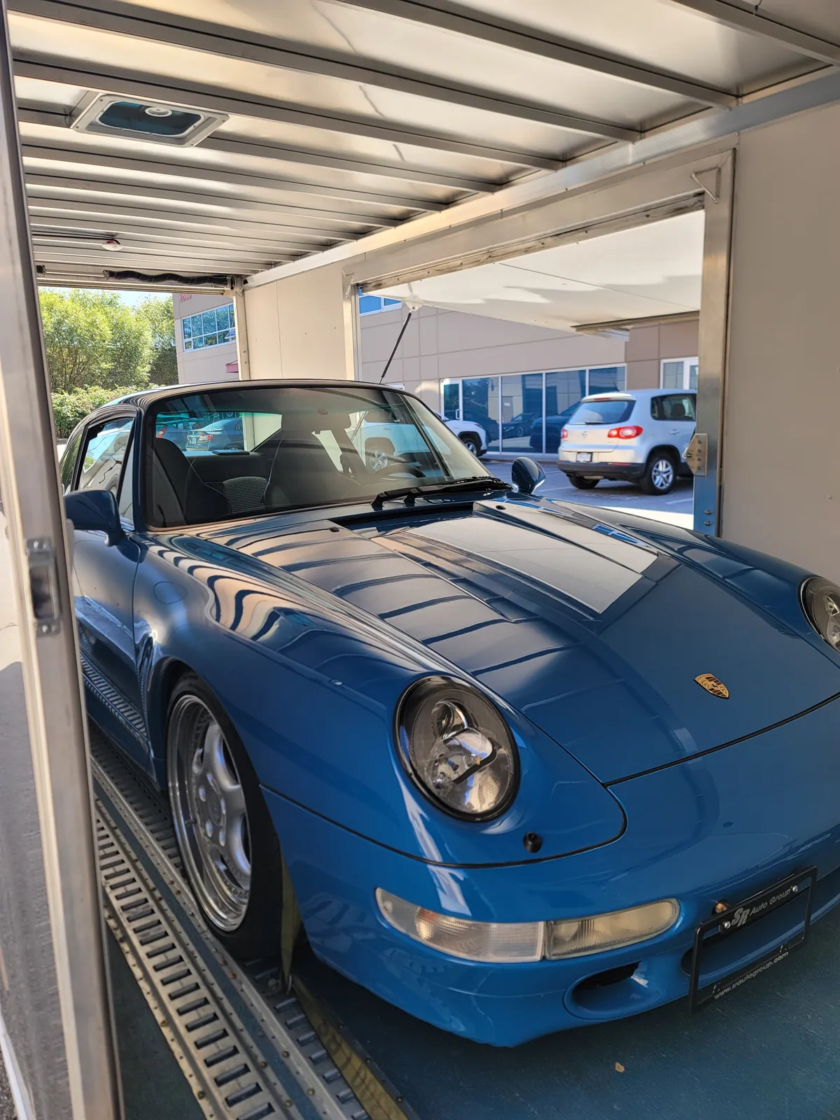 Blue Porsche 911 (993) loaded nose-out inside an enclosed transport trailer.