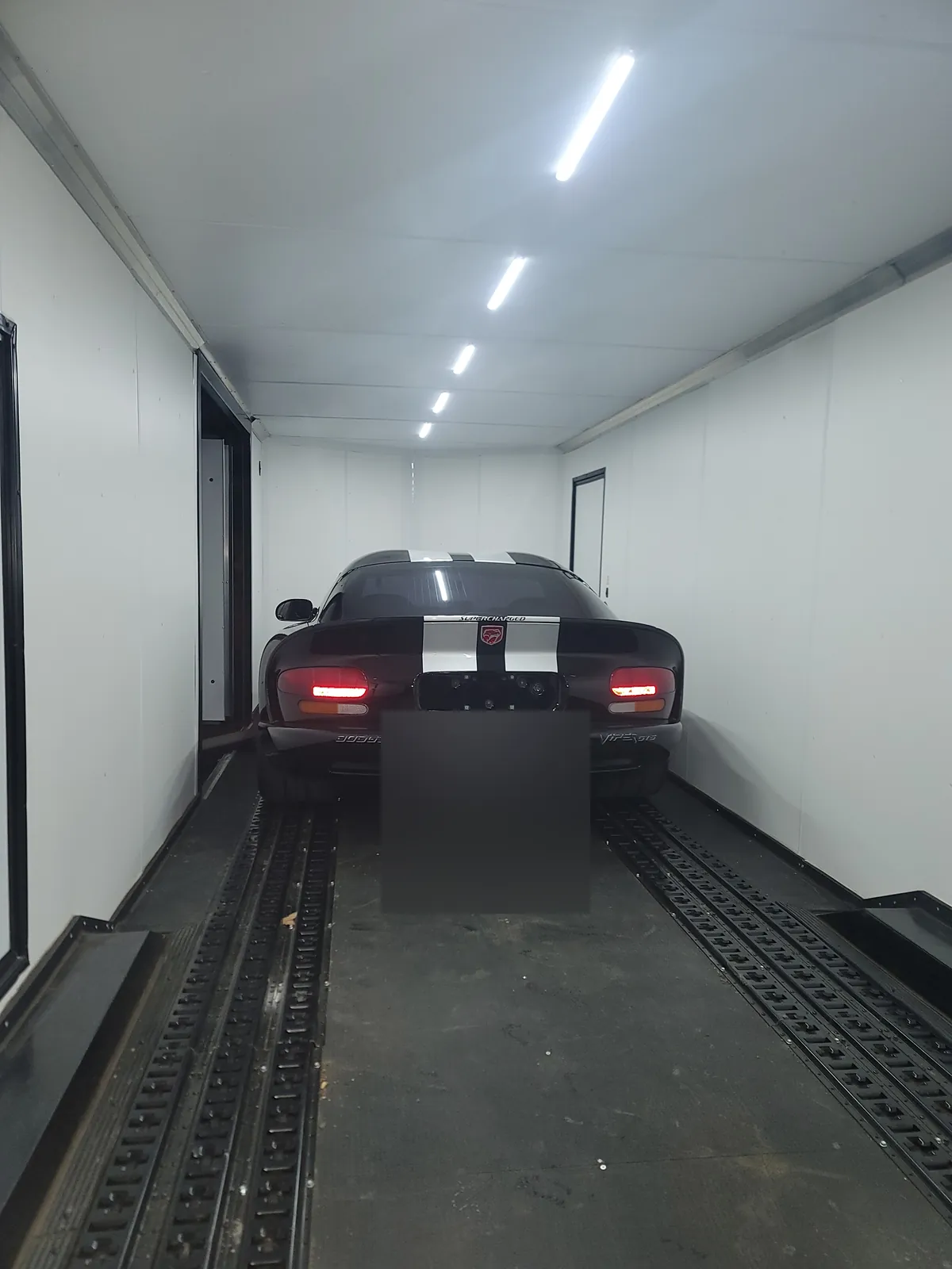 Black Dodge Viper secured with wheel straps inside an enclosed trailer.