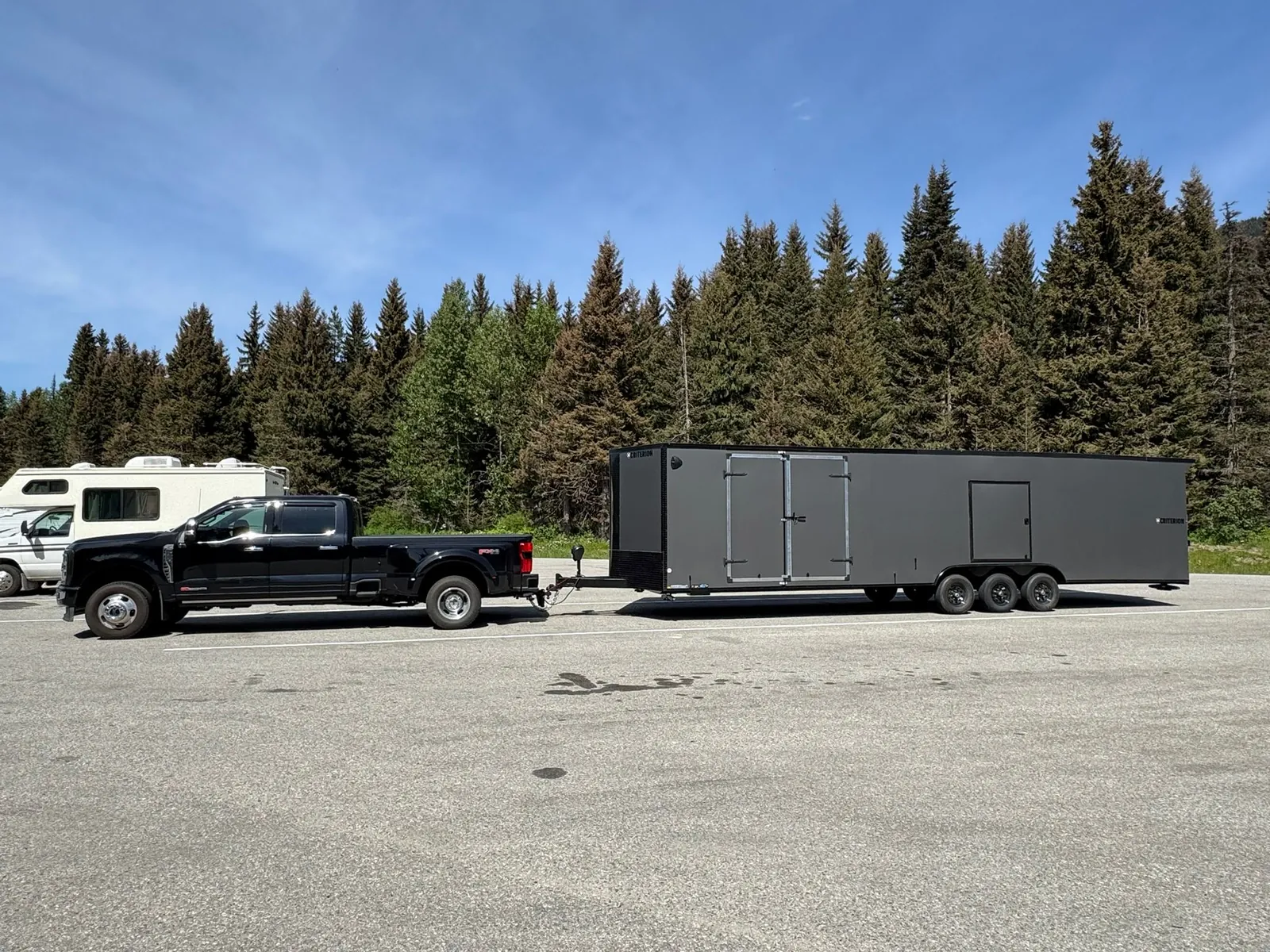 Coast2Coast truck and black enclosed trailer on a forested long-distance route.